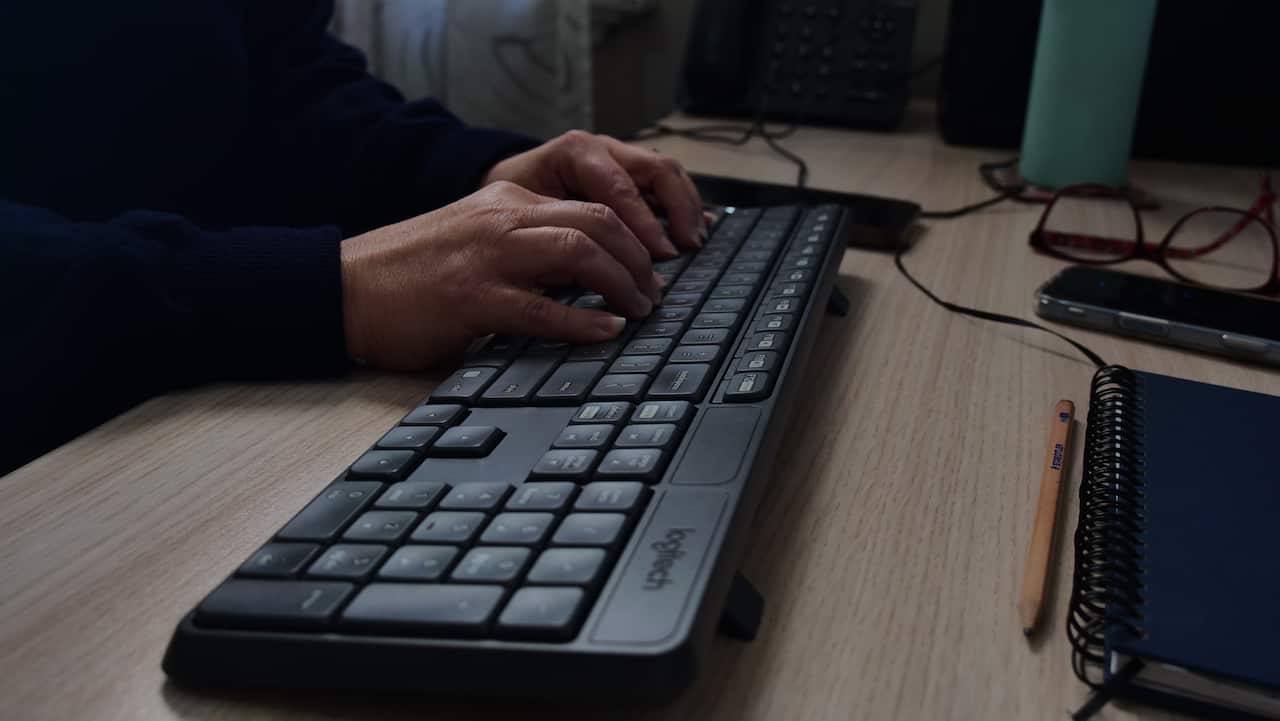 A close-up of a woman's hands typing on a keyboard placed on a wooden desk.