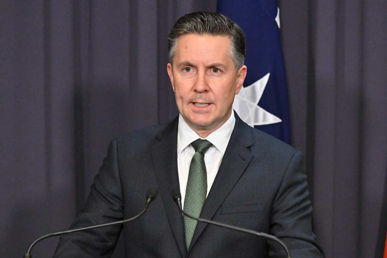 A man in a suit standing in front of microphones at a podium.