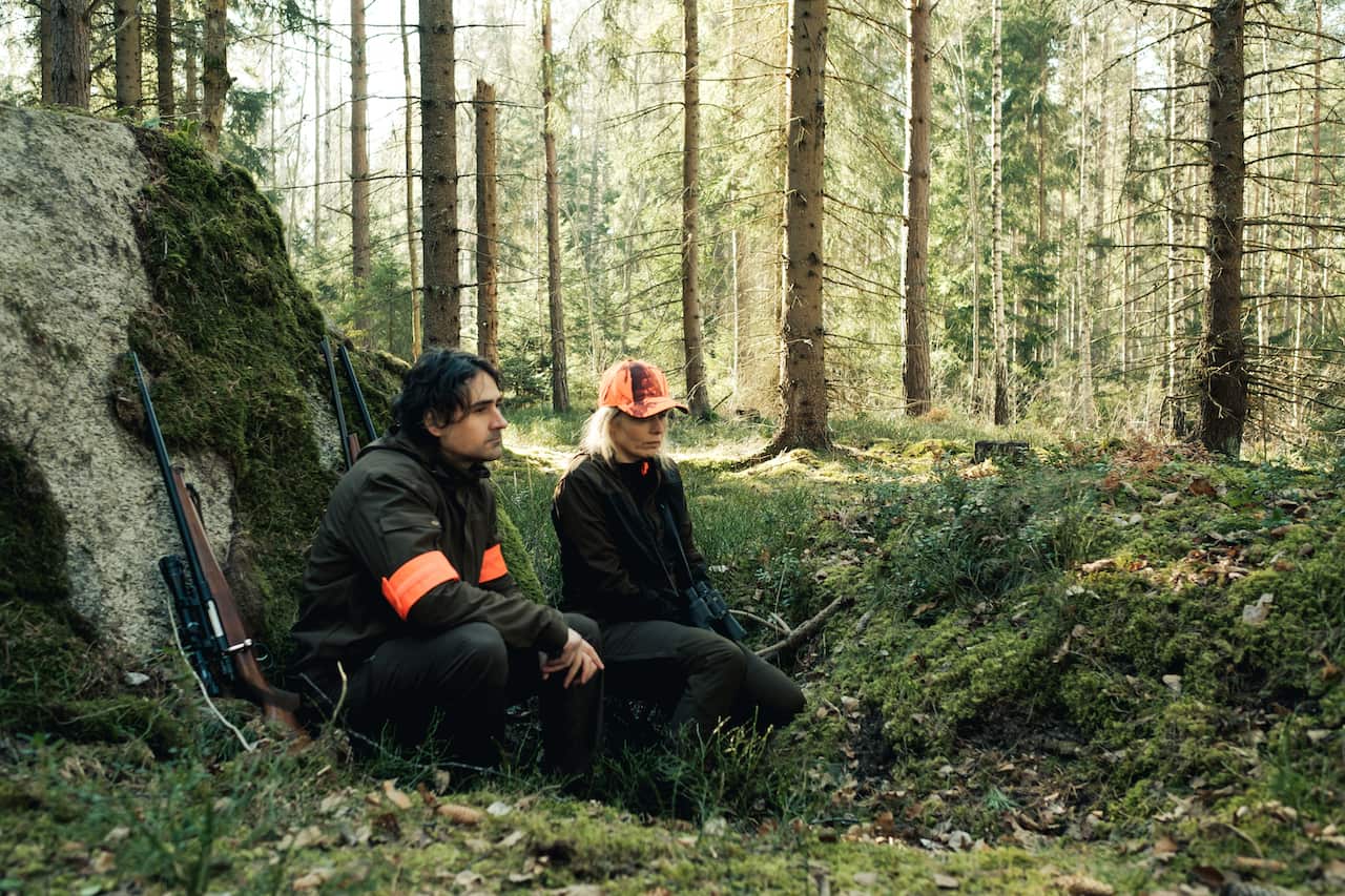 A man and woman rest in the forest. They have been hunting.jpeg