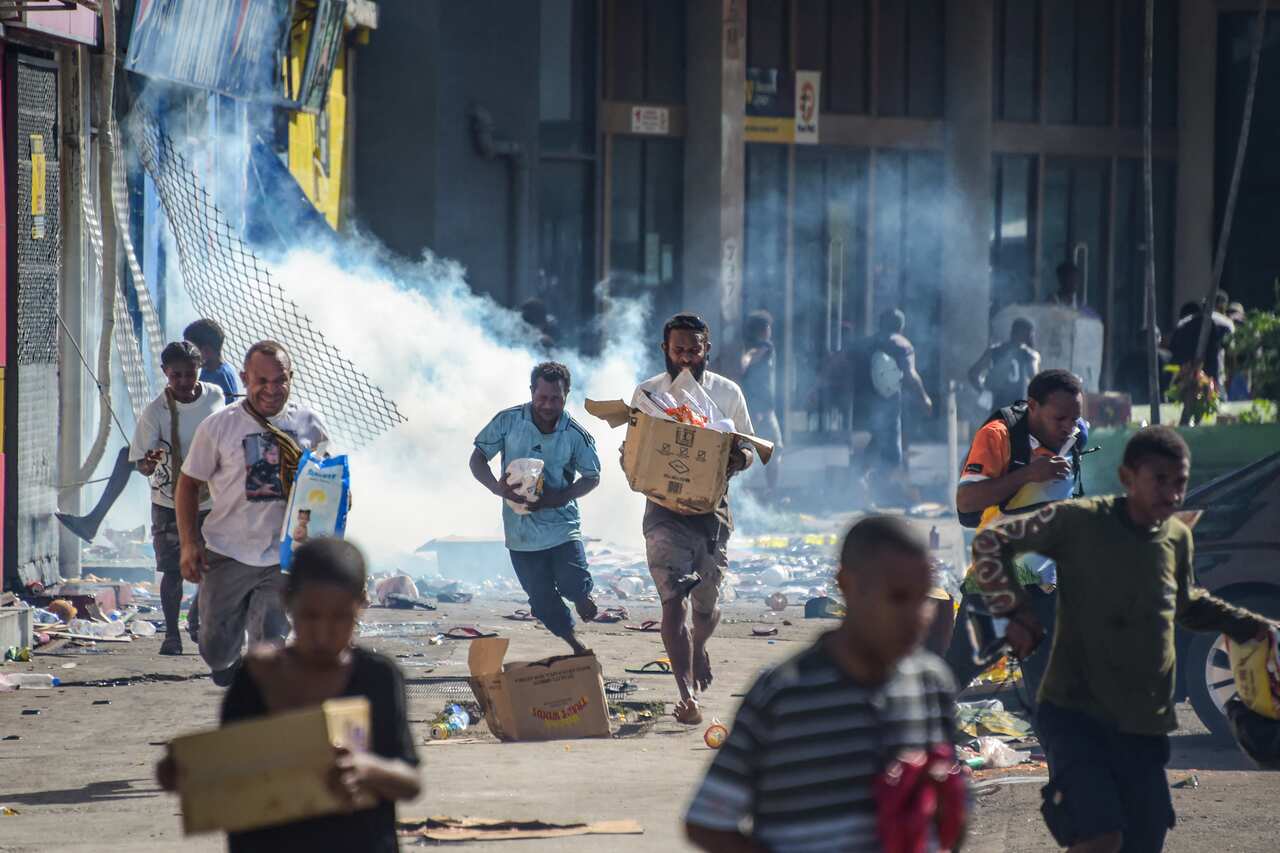 People running along a street. One is carrying a box.