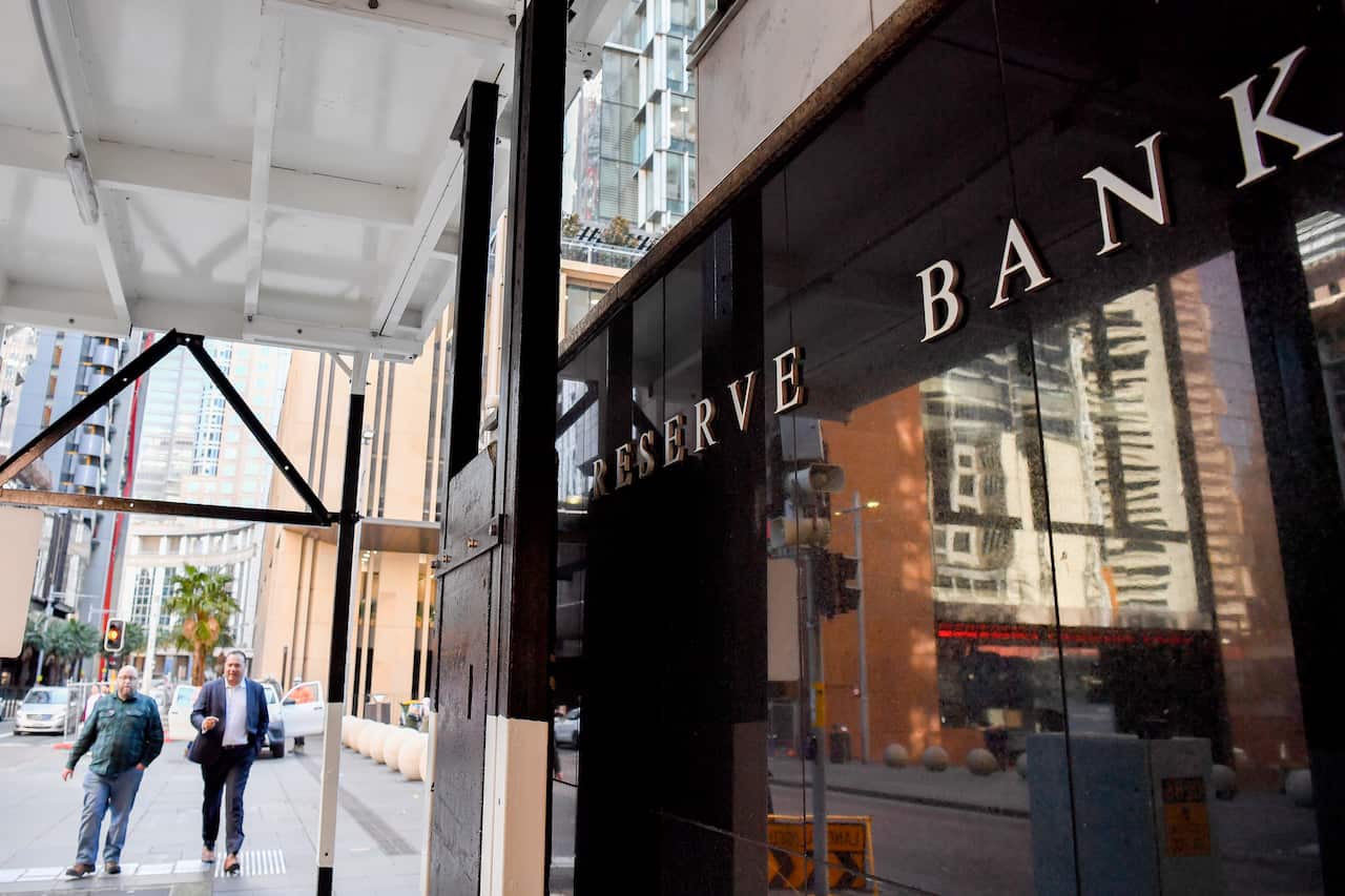 People walking down a street near a building with "Reserve Bank" written above it.