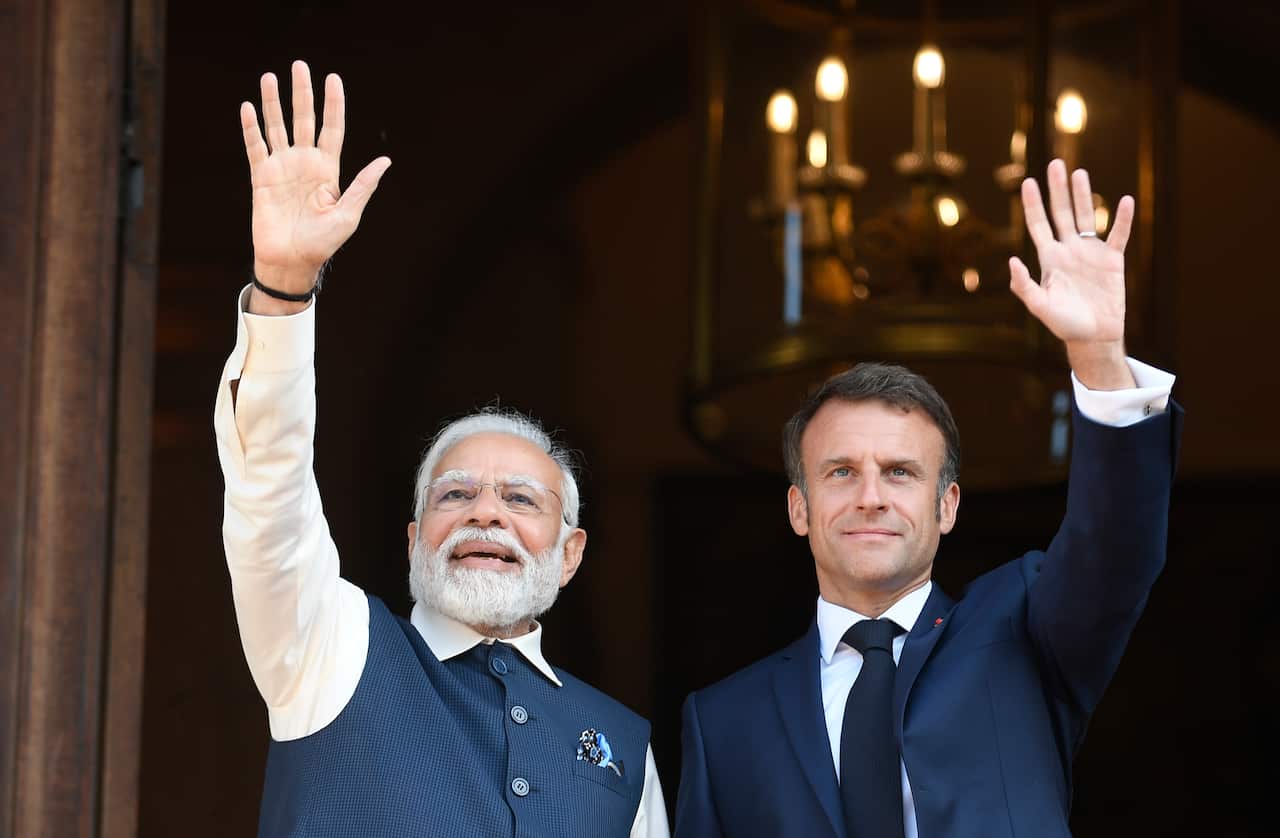 Narendra Modi and Emmanuel Macron wave at a crowd.