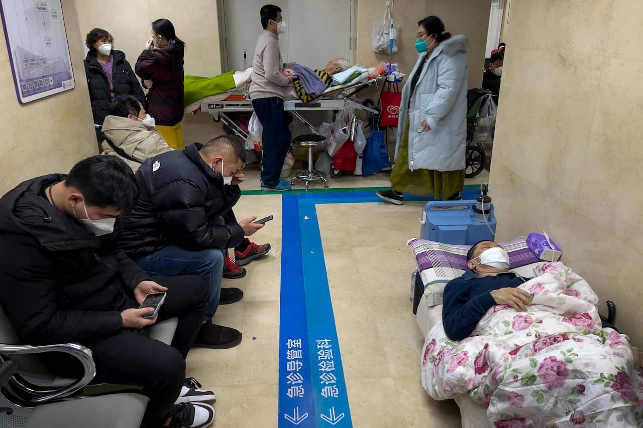 People sitting on chairs and a patient lying on a stretcher in a hospital hallway