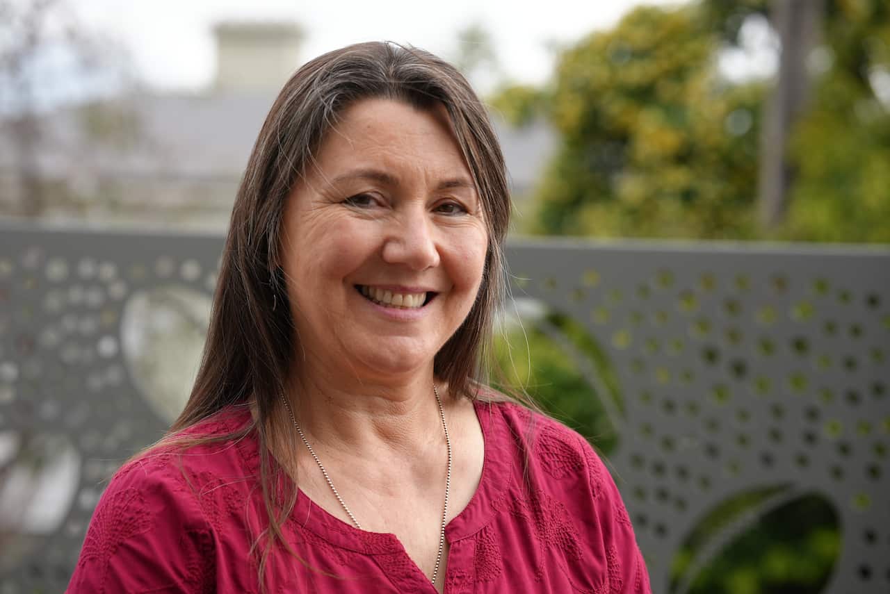 A woman in a red top and long brown hair smiles at the camera.