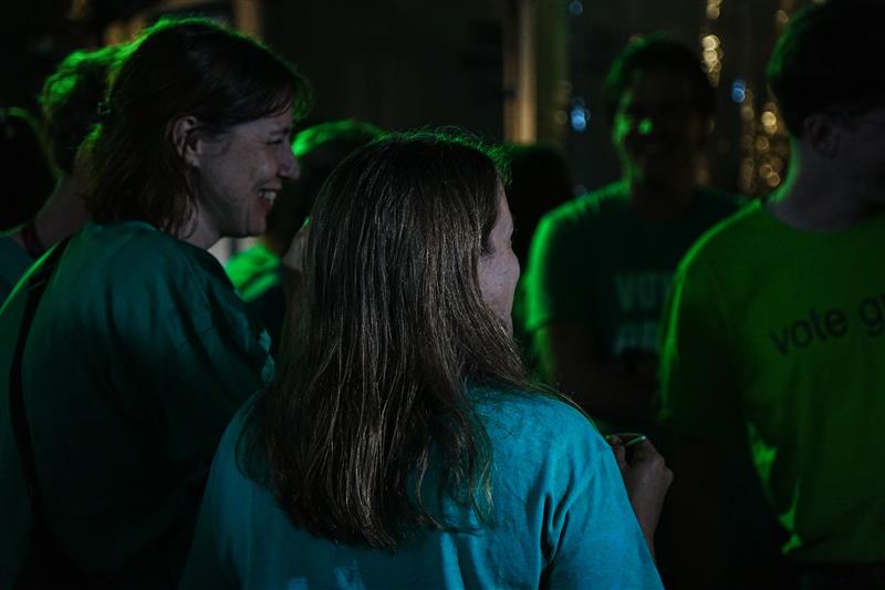 A group of people are in a dark room laughing and amiling together, there are green lights and green t-shirts. 