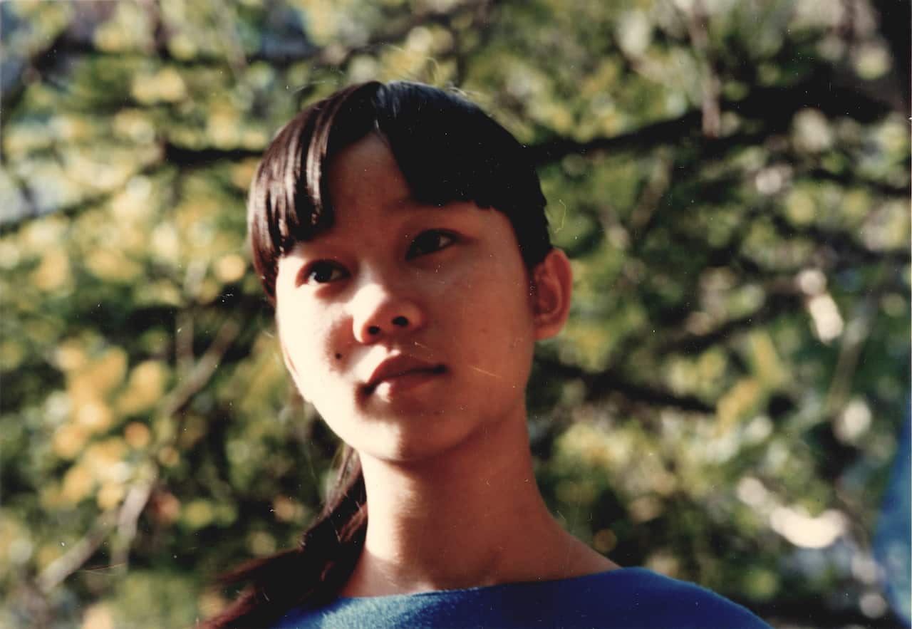 A young Chinese woman standing outside beside trees.