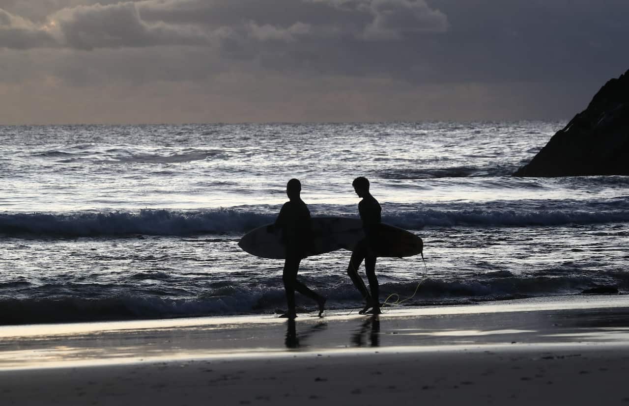 Two people holding surfboards on a beach walking towards the water.