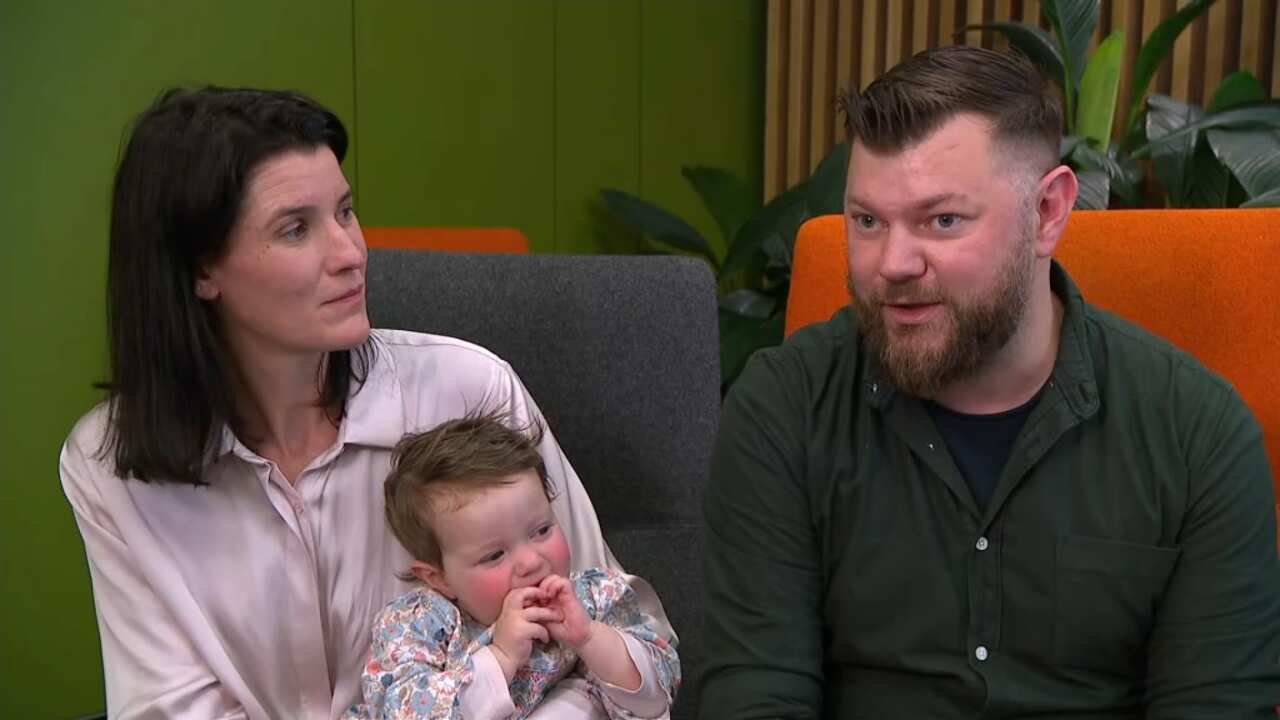 A woman holding a toddler looks at the man sitting next to her as he speaks