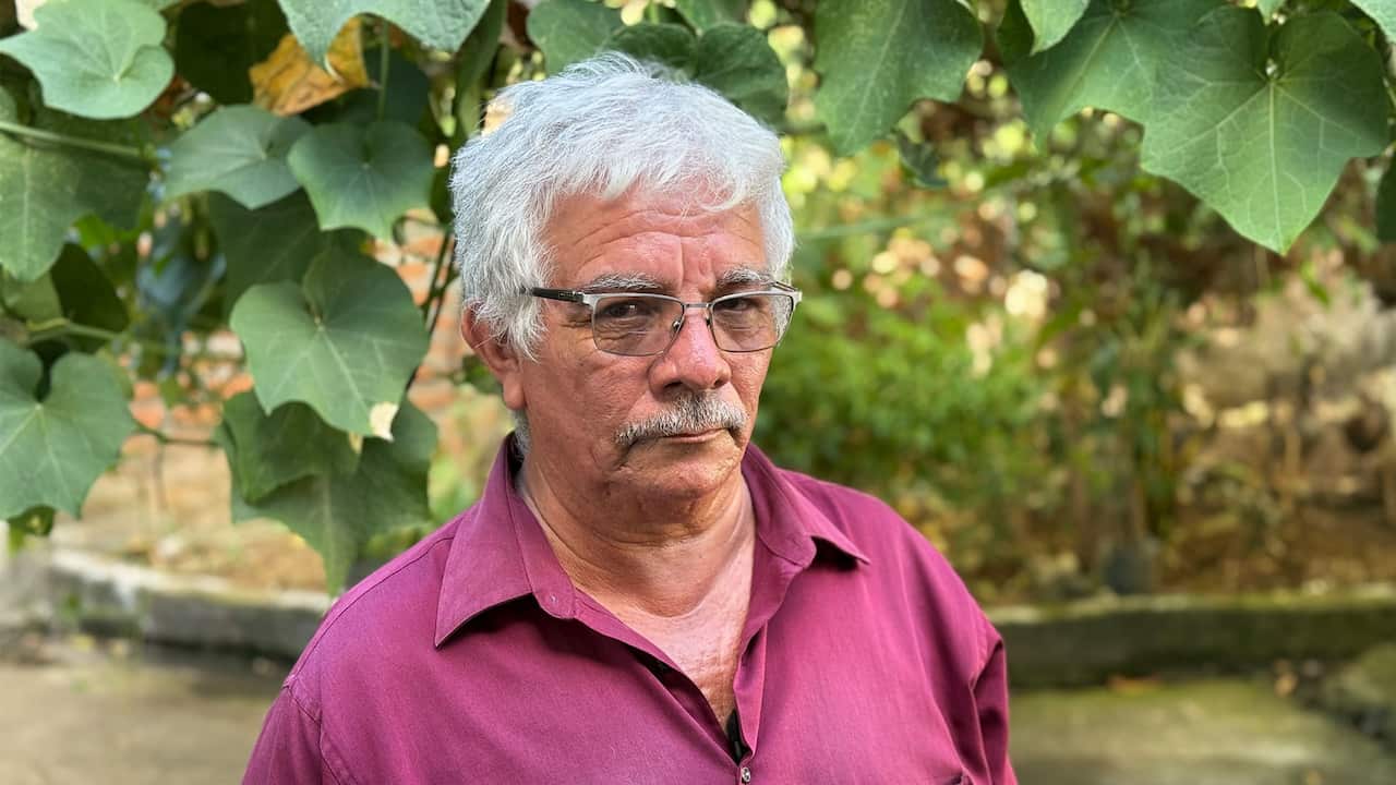  A grey-haired, moustachioed, and bespectacled man wearing a burgundy shirt
