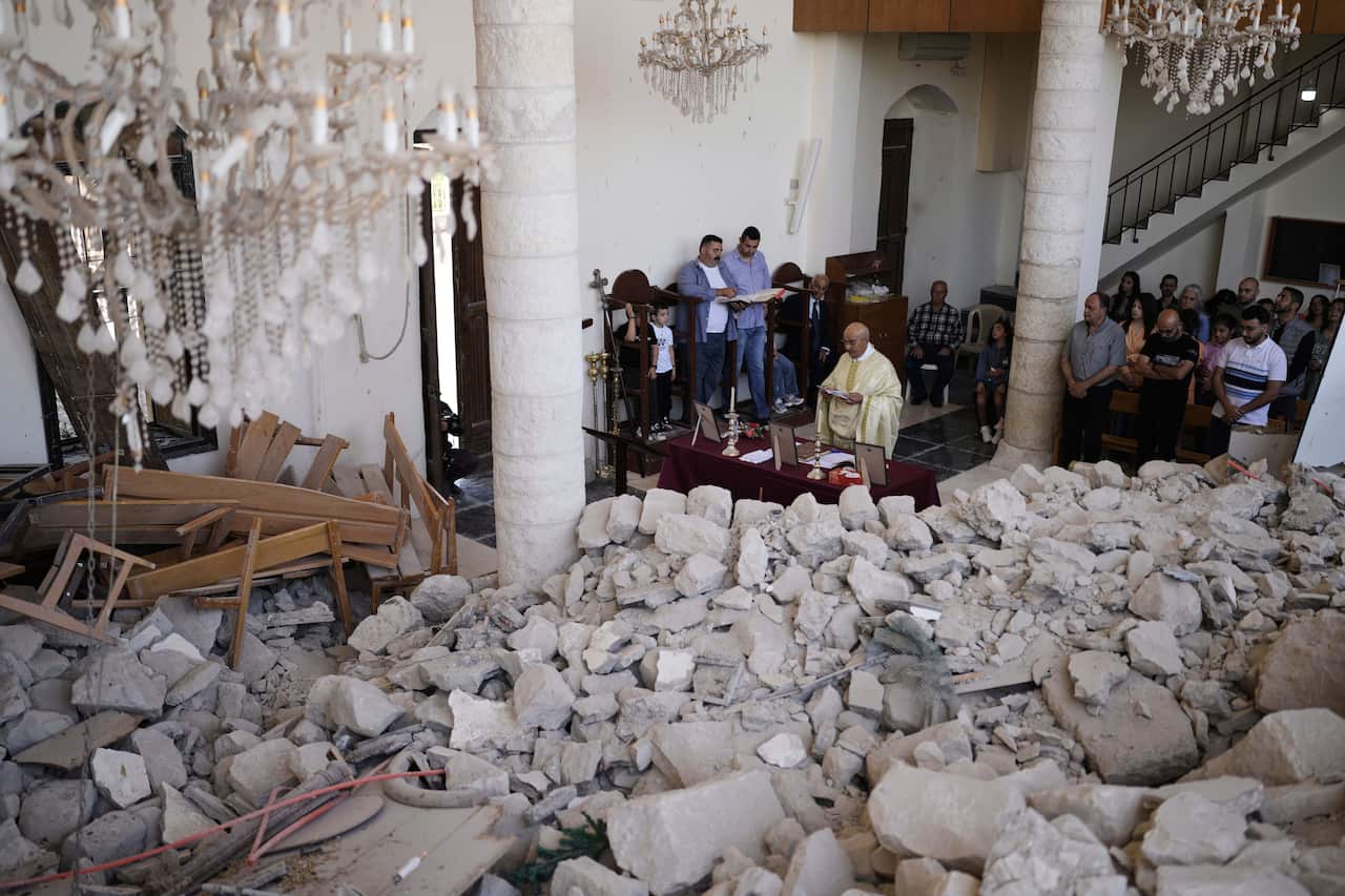 A priest leads a small congregation in prayer inside a building filled with rubble. 
