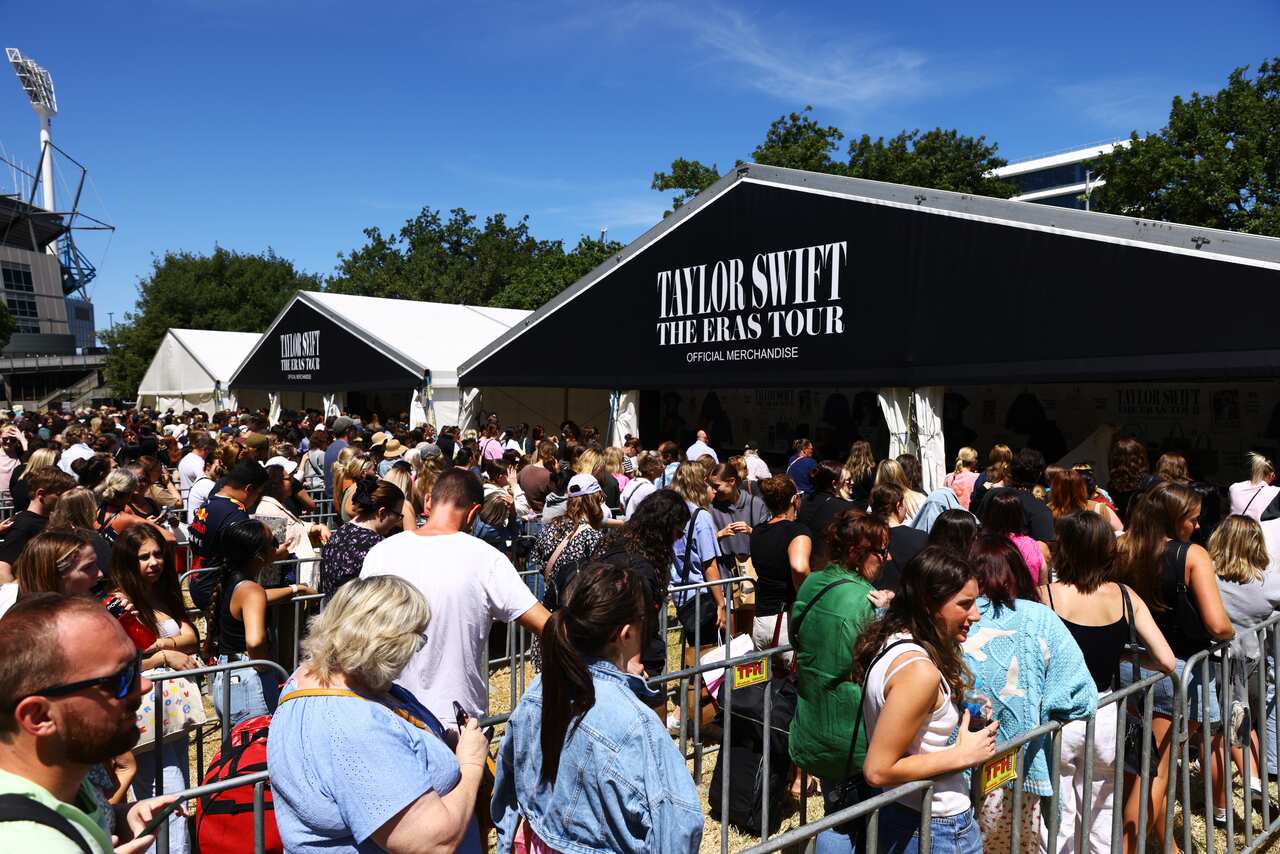 Long lines of people divided by the metal temporary fences in front of the stalls with the sign Taylor Swift's official Eras tour merchandise.