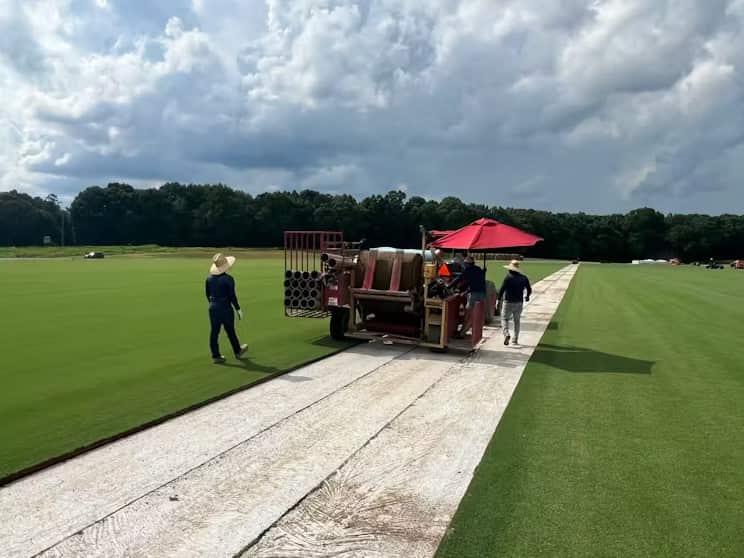 Ground staff lay down turf with a machine at a stadium