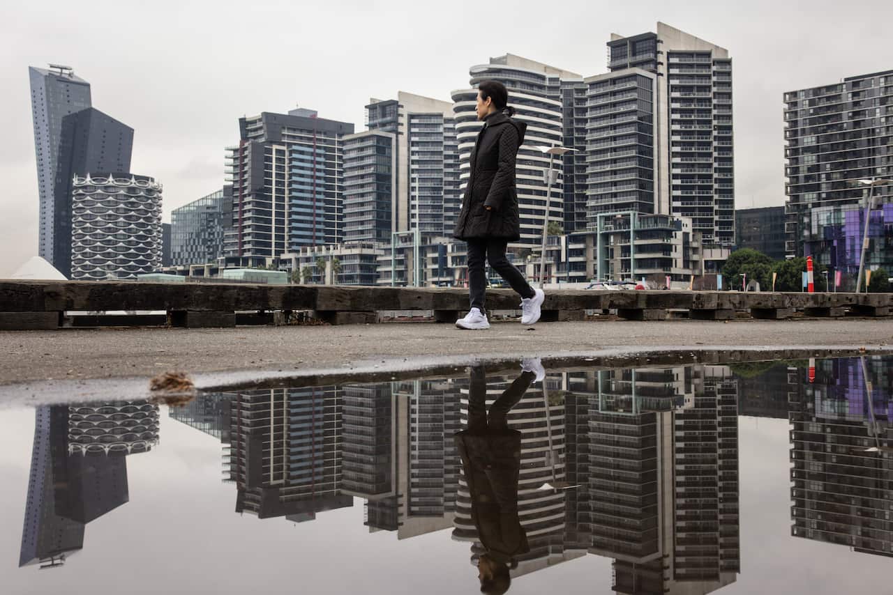 A woman in black winter clothes walks past the Melbourne sky line on a cold morning.