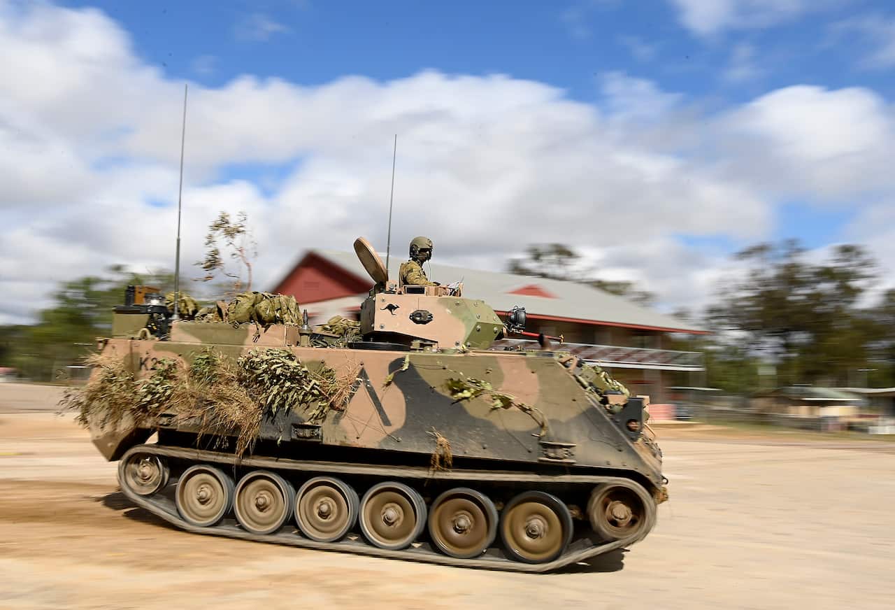 A soldier atop an army tank on a dirt road.
