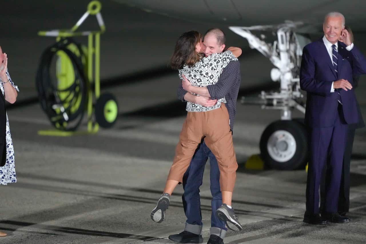 A woman in brown pants in raised in the air as she hugs a smiling younger man.