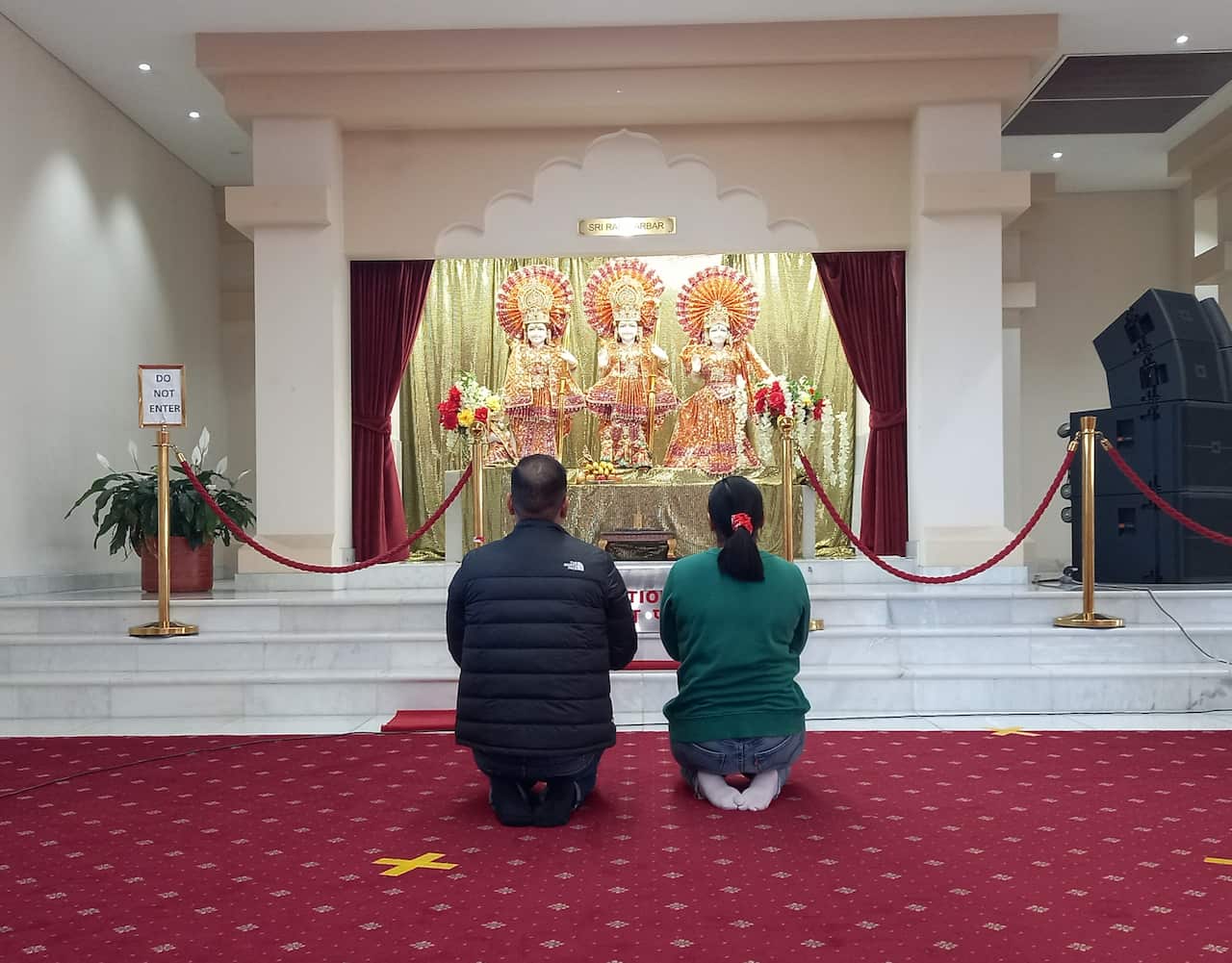 Two people kneel in prayer inside a Hindu temple.