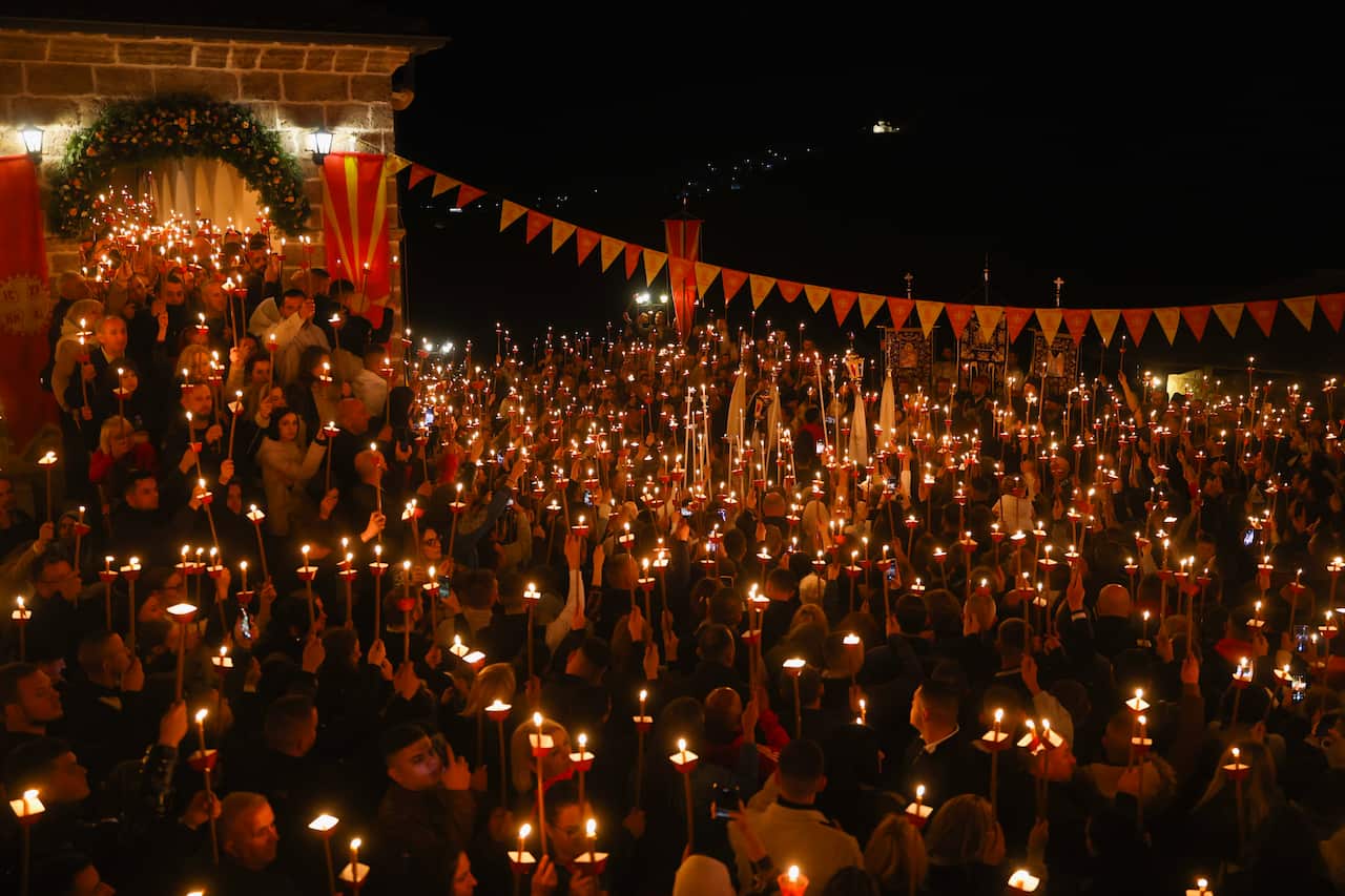 A crowd of people holding lit candles gather outside in the night for Orthodox Easter celebrations.