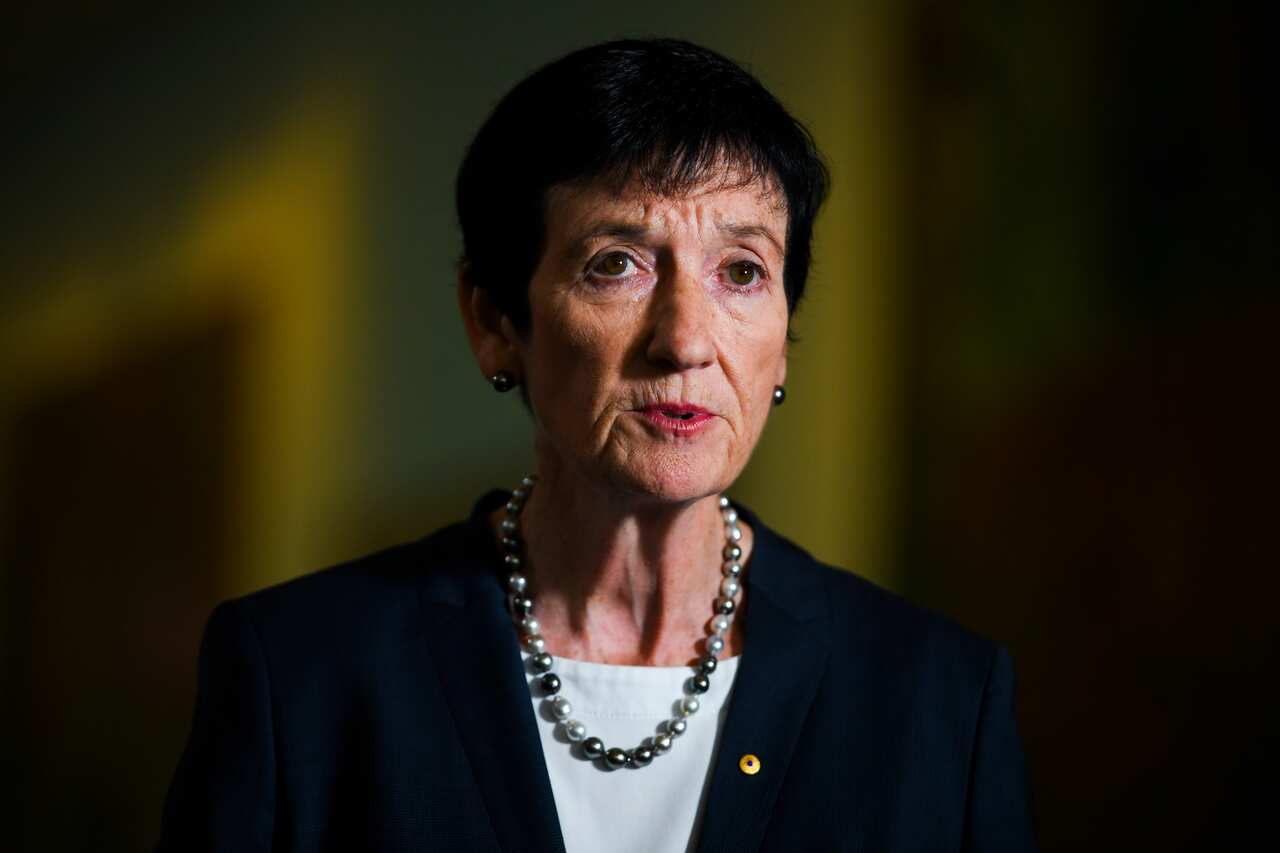 A woman in a black blazer and pearl necklace.