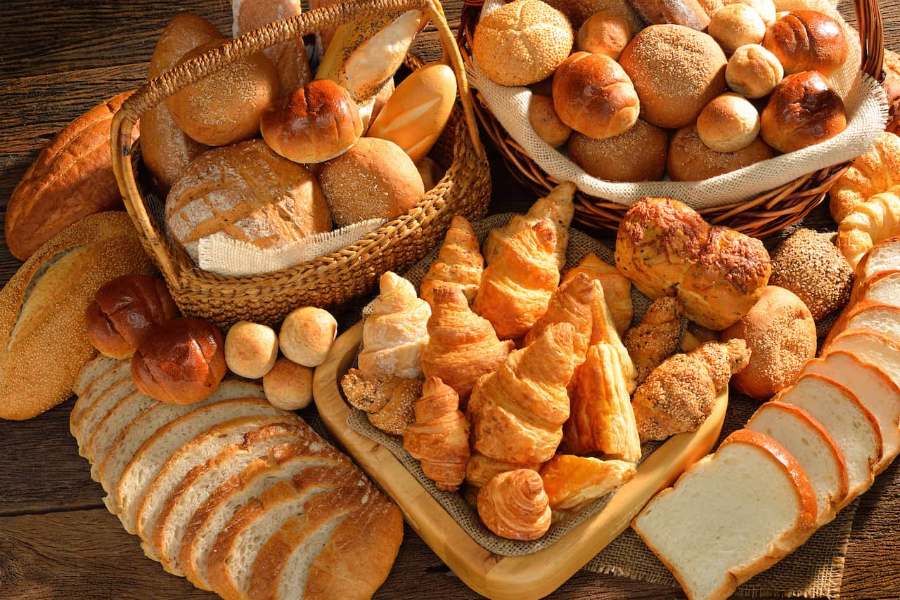 Variety of bread in wicker basket on old wooden background.