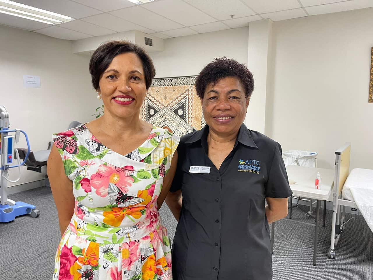 A woman in a colourful dress (left) standing next to a woman wearing a dark grey shirt