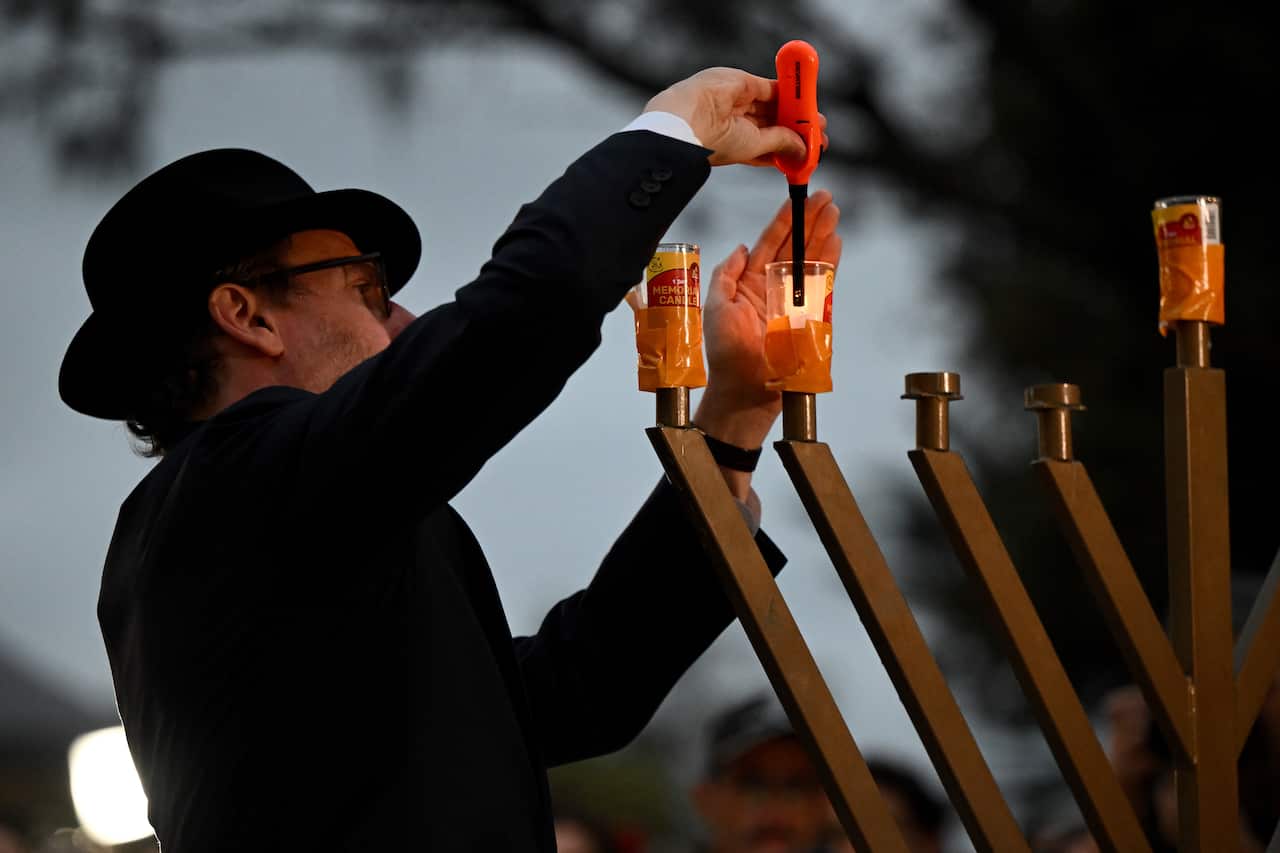 A rabbi in black clothes lights a menorah during a vigil.