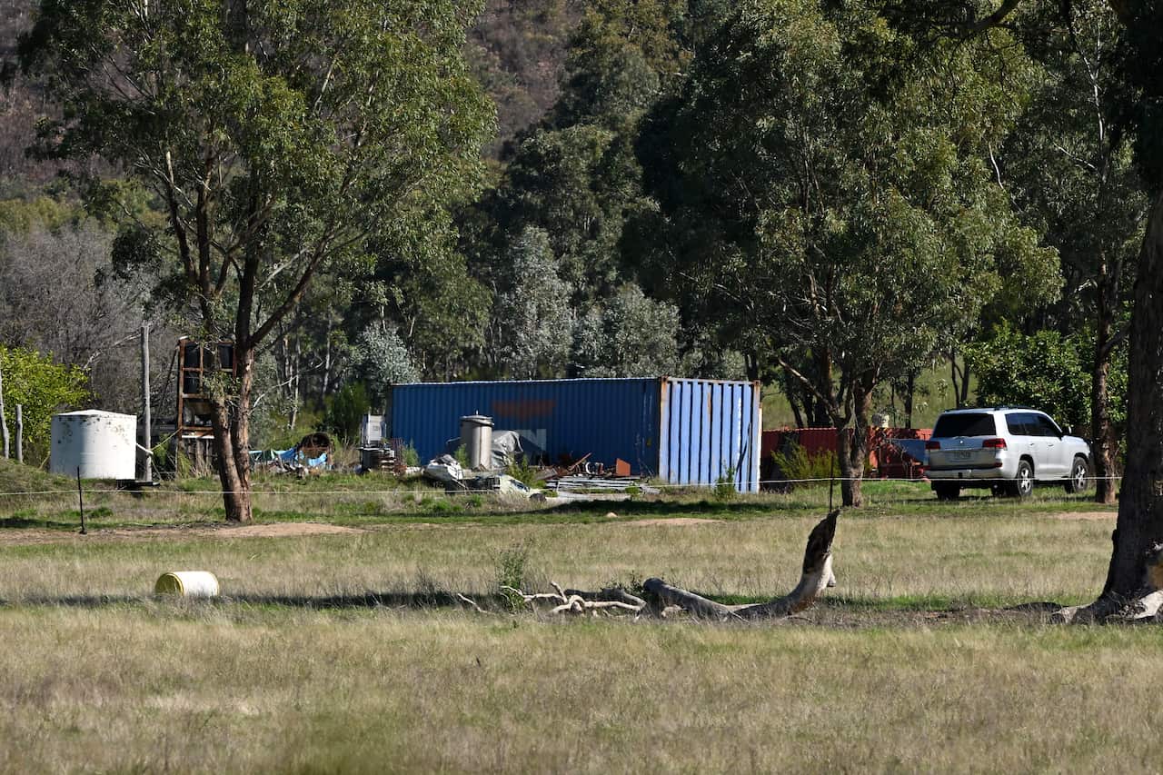 Shipping containers and vehicles among trees in bushland.