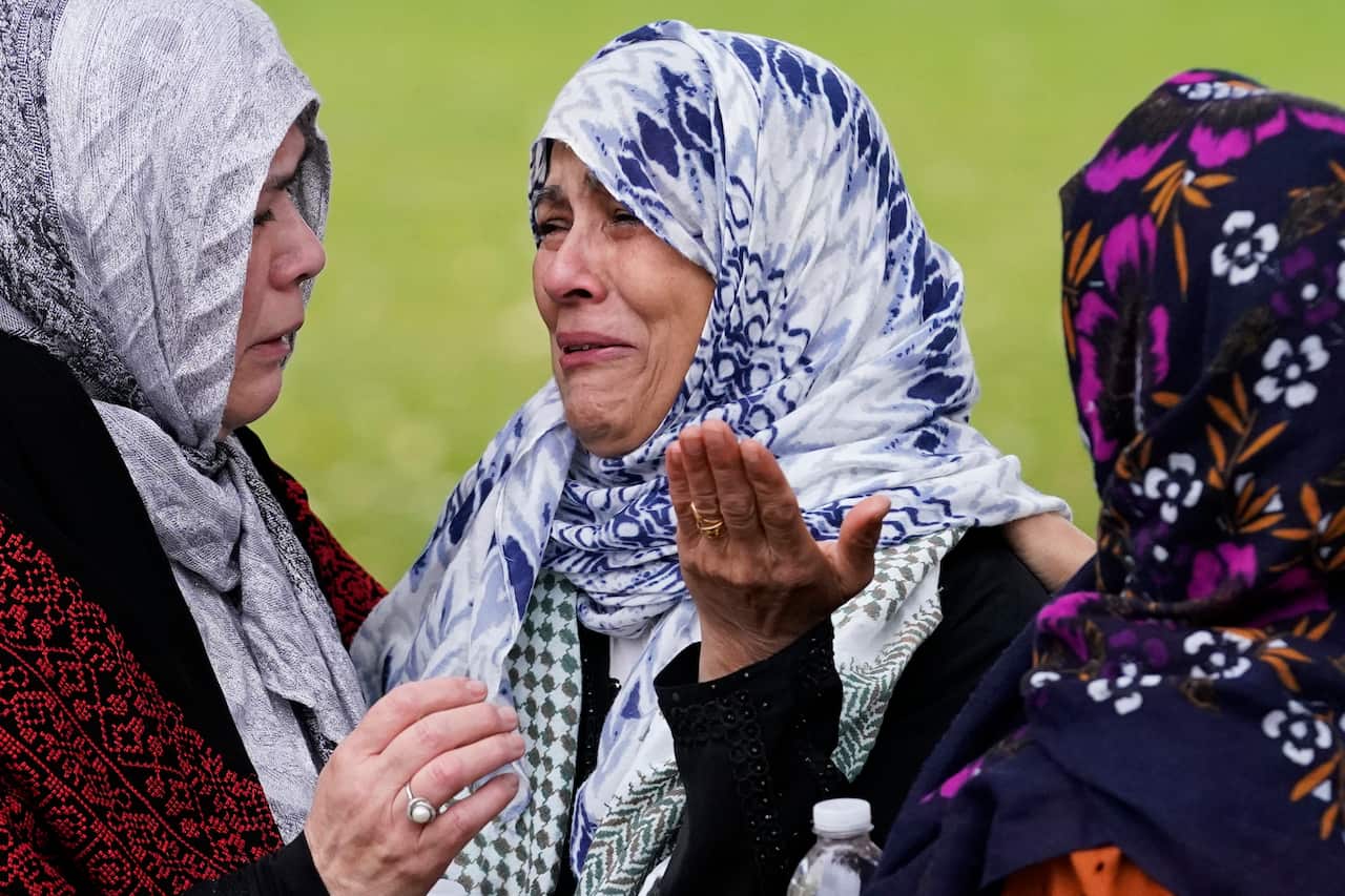 Muslim women wearing headscarves of various colours cry and comfort one another.