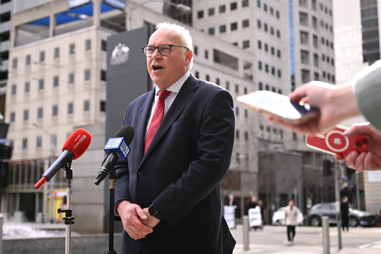 A man in a blue suit and tie speaks in front of two microphones.
