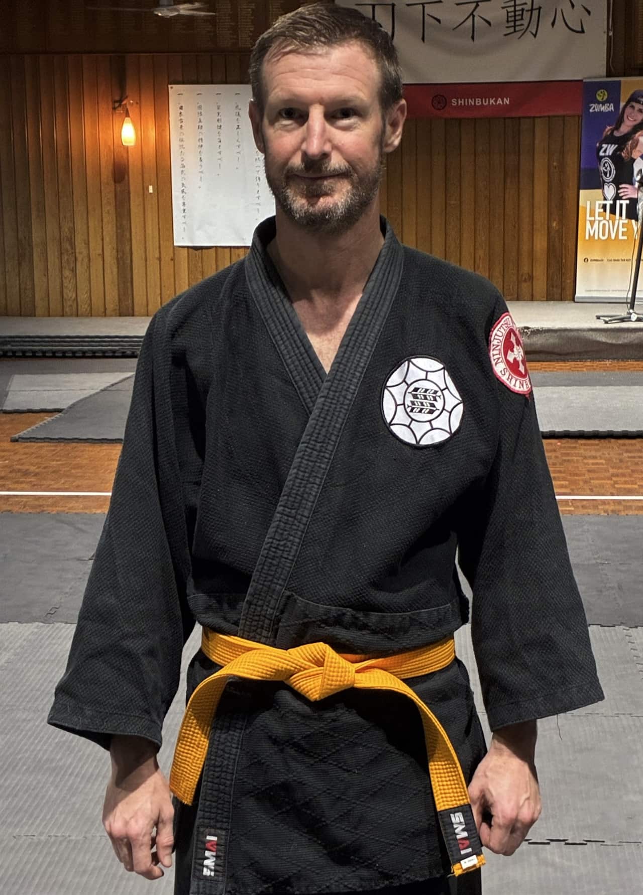 A man wearing black karate clothing and a yellow belt stands facing camera.