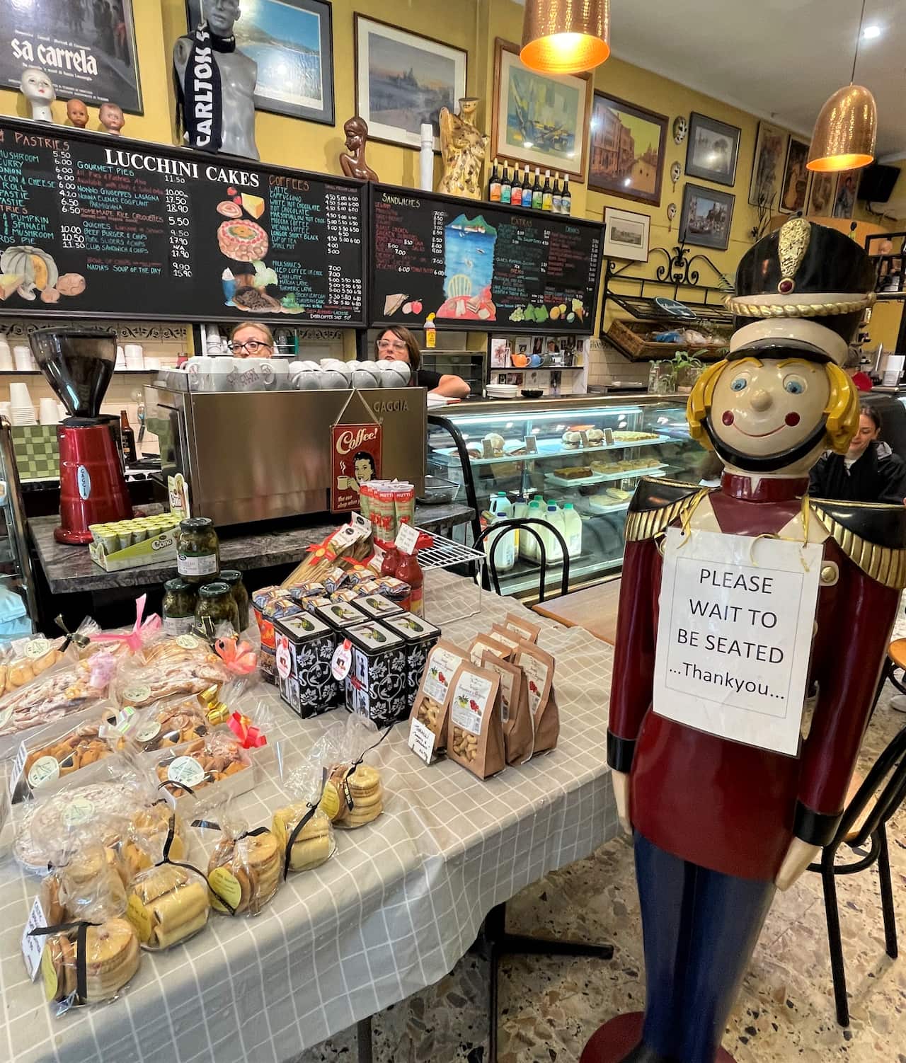 A cake shop showing shelves of biscuits and cakes, paintings and a toy soldier.
