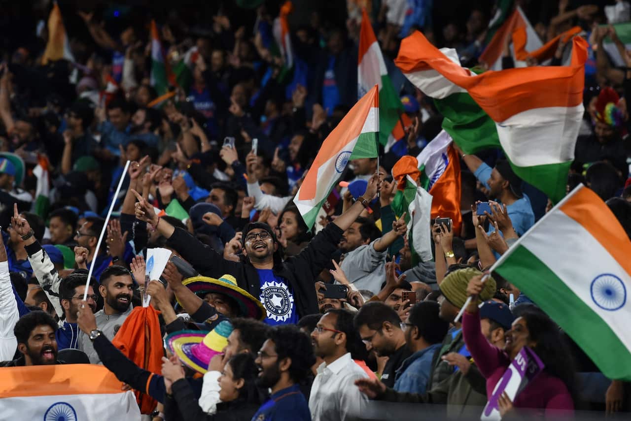 A section of a crowd at the cricket. A number of people are waving Indian flags