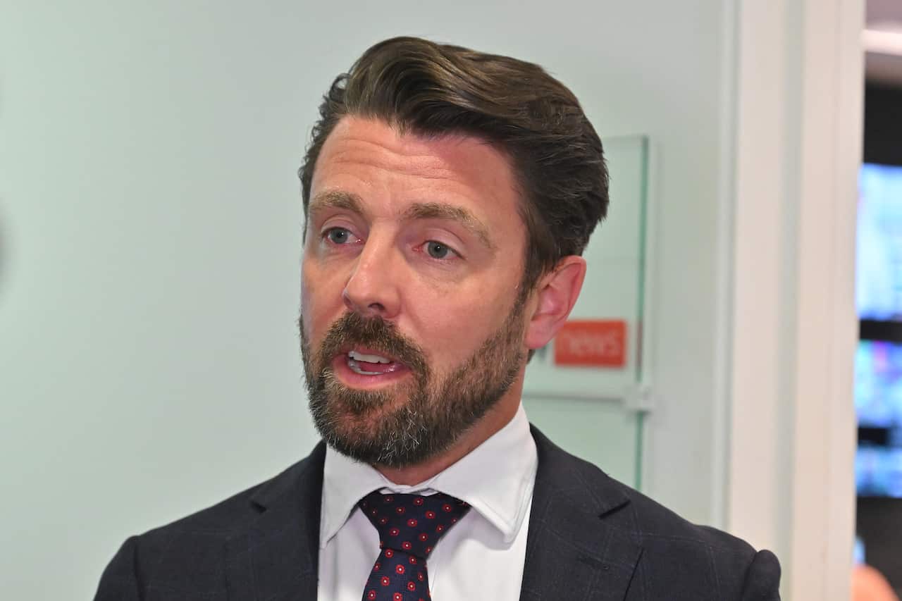 A man in a suit addresses the media with a serious expression on his face.