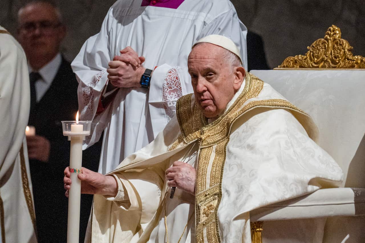 Seated man in white and gold robes holds an Easter candle during the Easter Vigil