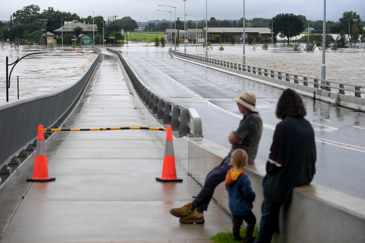 People observing a bridge that is impacted by floodwater