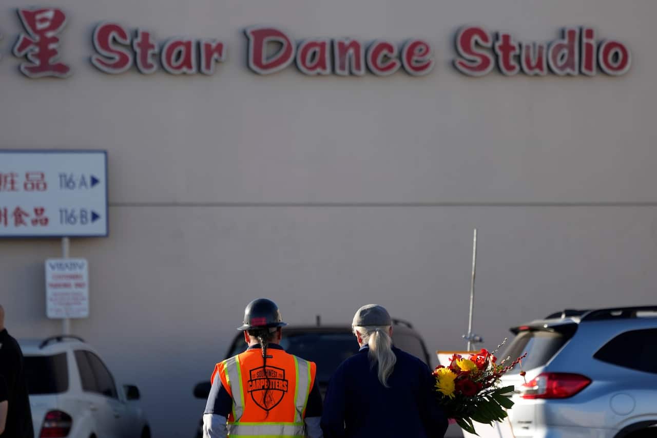 Two men walk to the Star Ballroom Dance Studio holding flowers on Monday, Jan. 23, 2023, in Monterey Park, Calif.