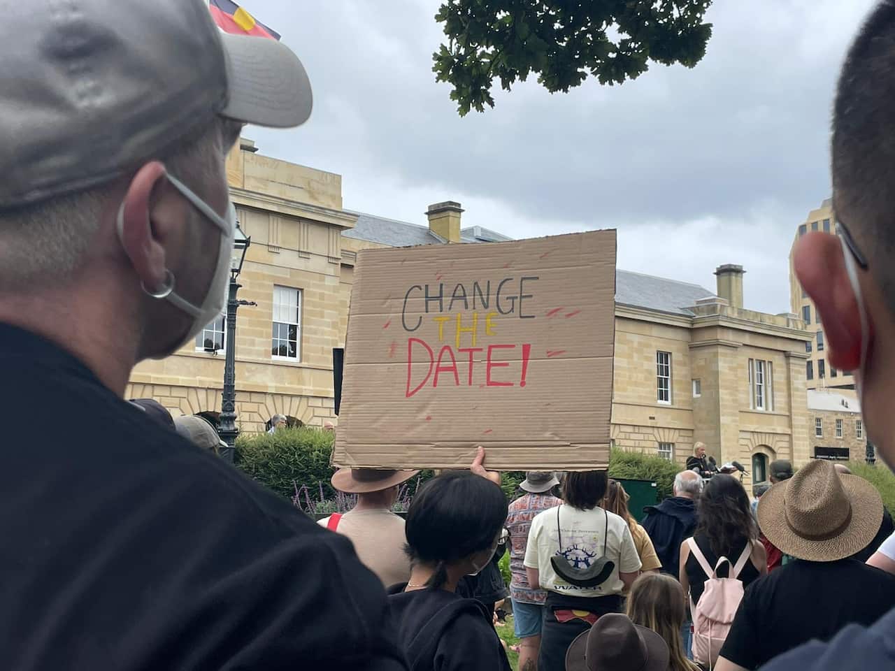 A protestor holds a handmade sign which reads 'Change The Date' at rally in Hobart (nipaluna)
