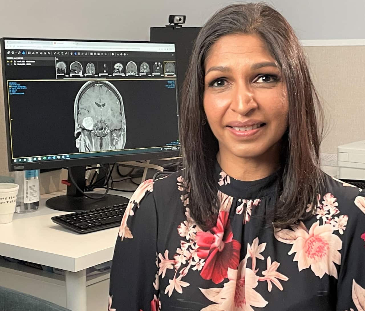 Dr Brindha Shivalingham sitting in her office in front of a brain sacn.
