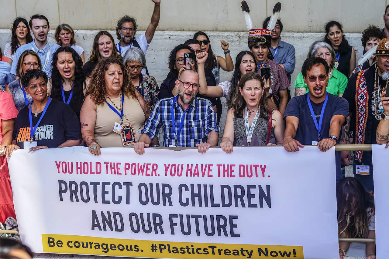 People standing behind a large white banner that has writing on it reading Protect our children and our future