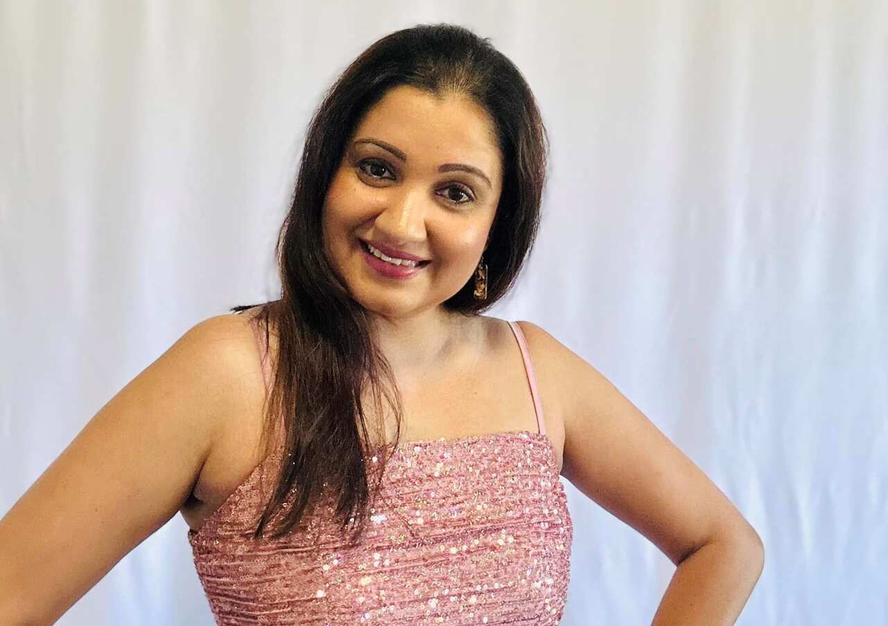 A woman wearing a pink sparkly top smiles at the camera