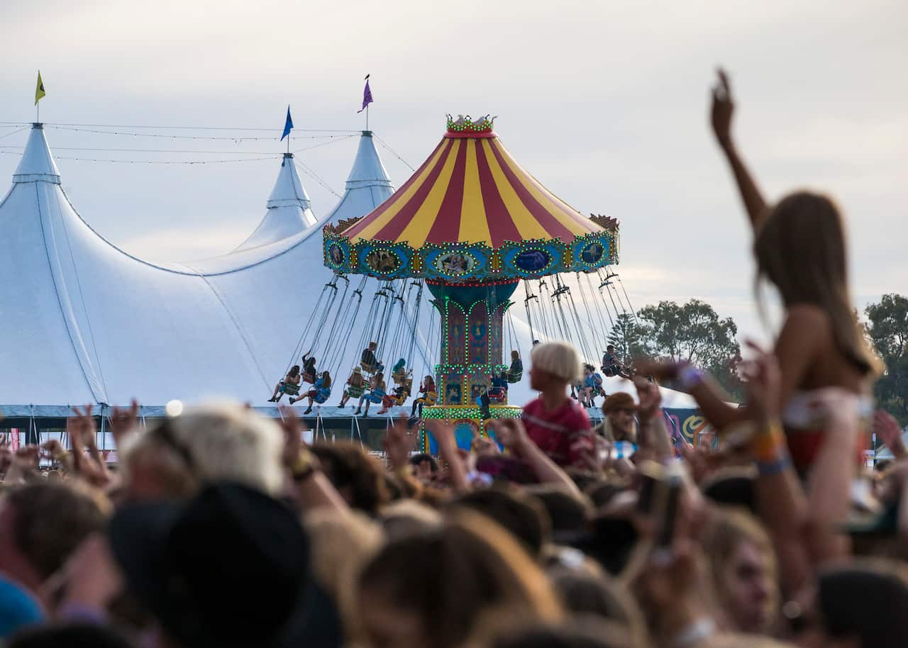 A crowd cheering. In the background is a large tent and a carnival ride.