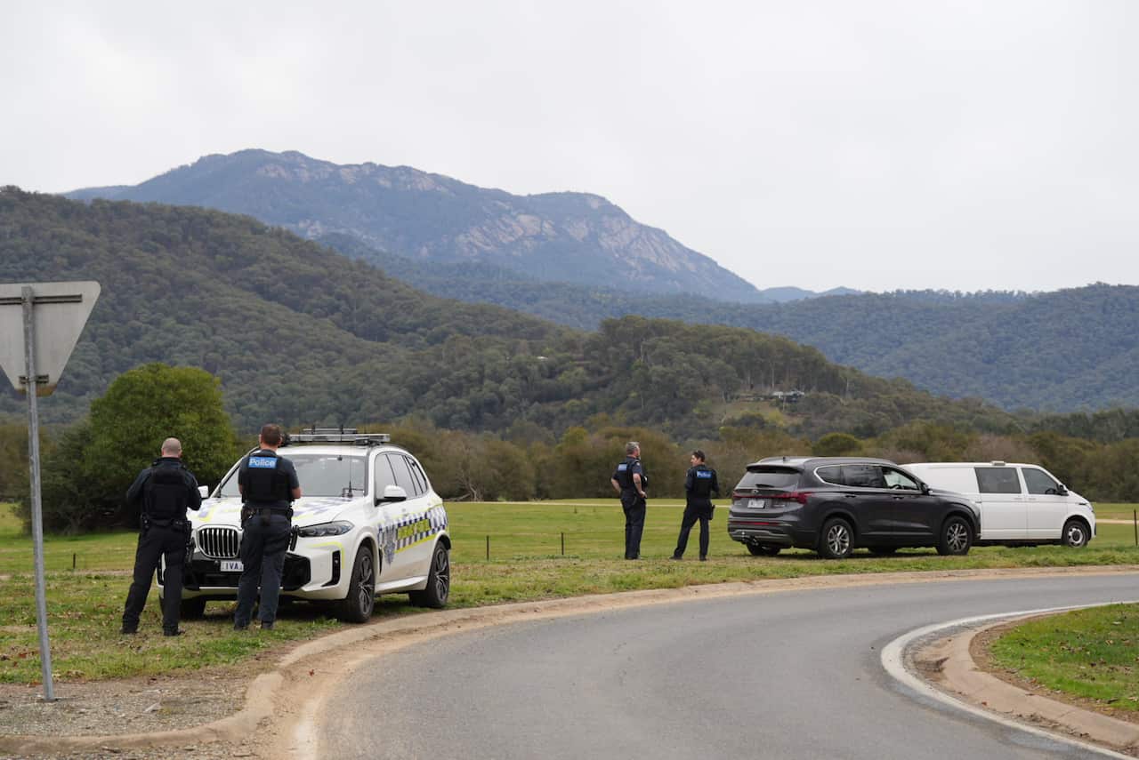 Police standing near vehicles at a large grassy area.