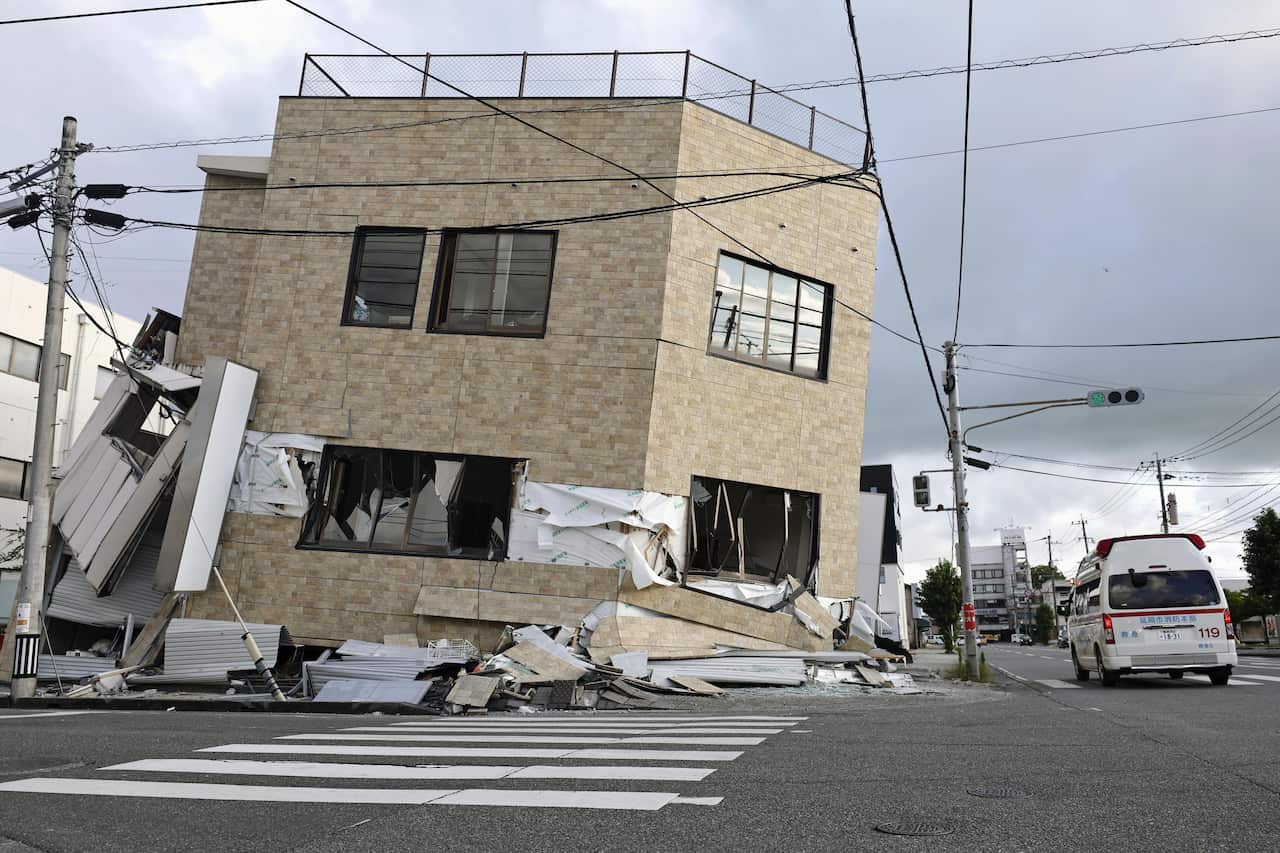 An emergency vehicle passes a partially collapsed brick building.