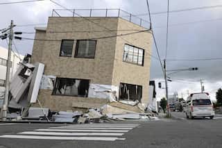 An emergency vehicle passes a partially collapsed brick building.