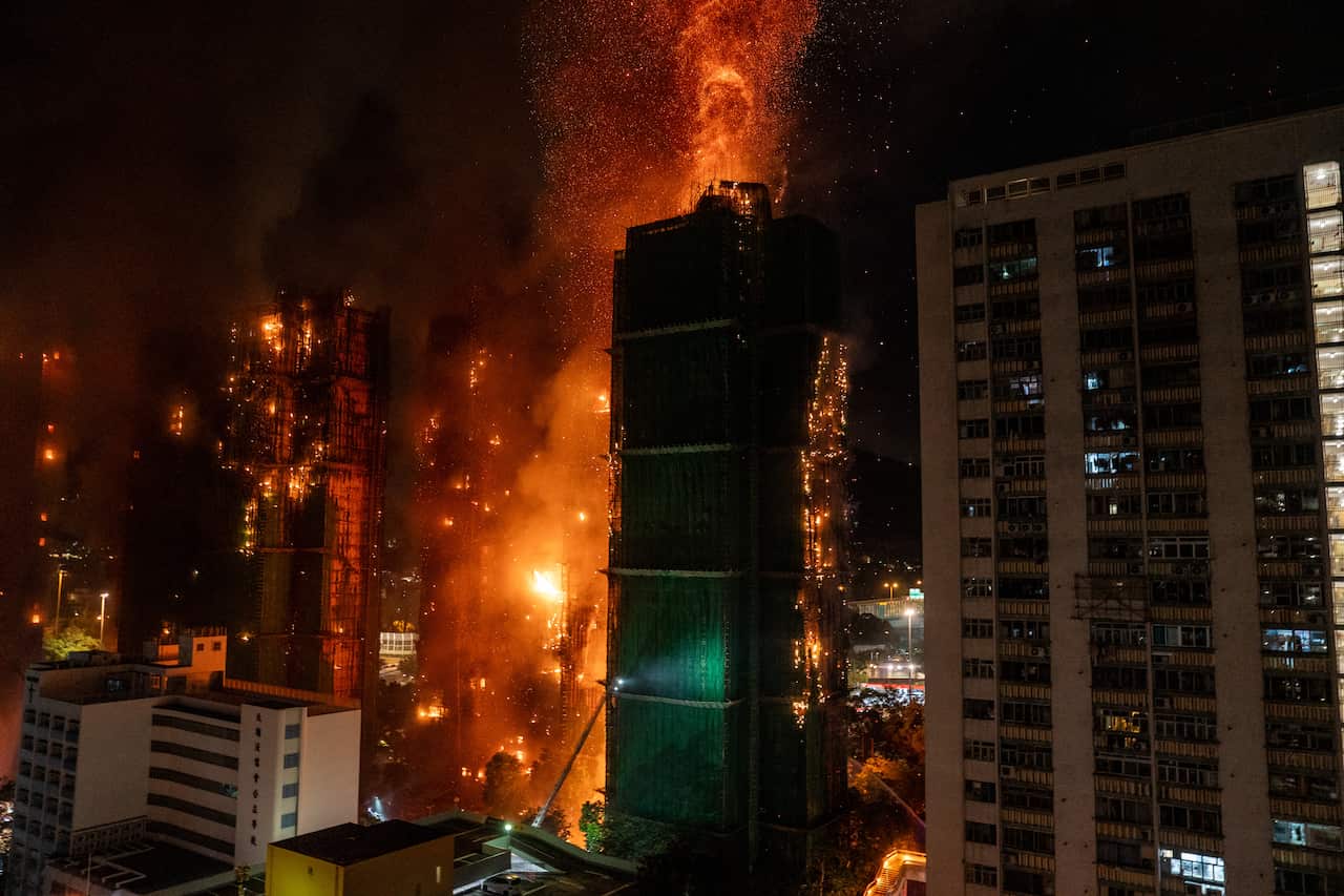 A building complex that has gone up in flames, amid other buildings.