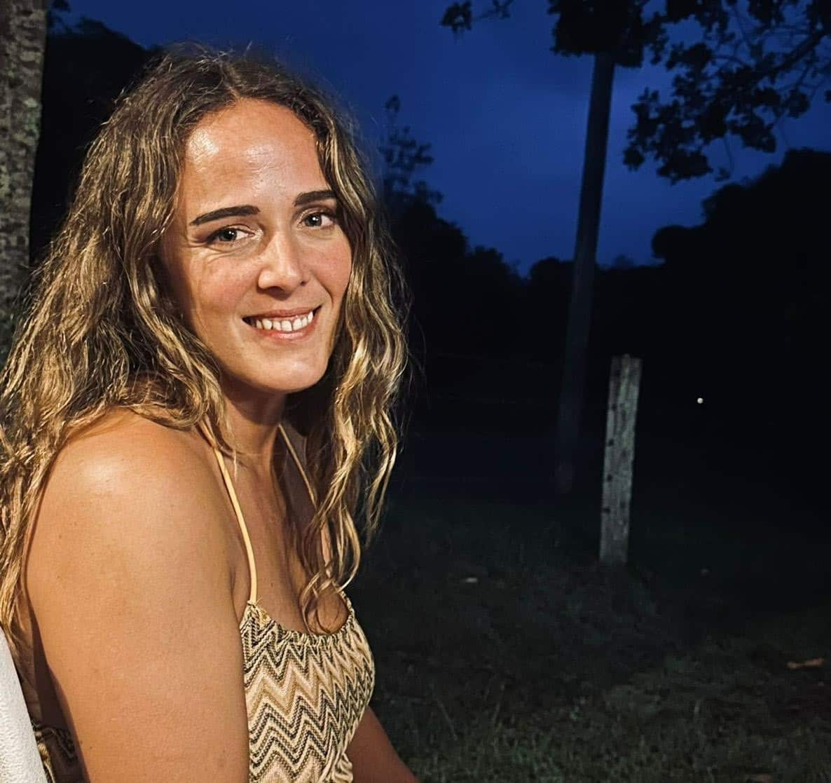 A woman sitting outside in the evening smiling at camera