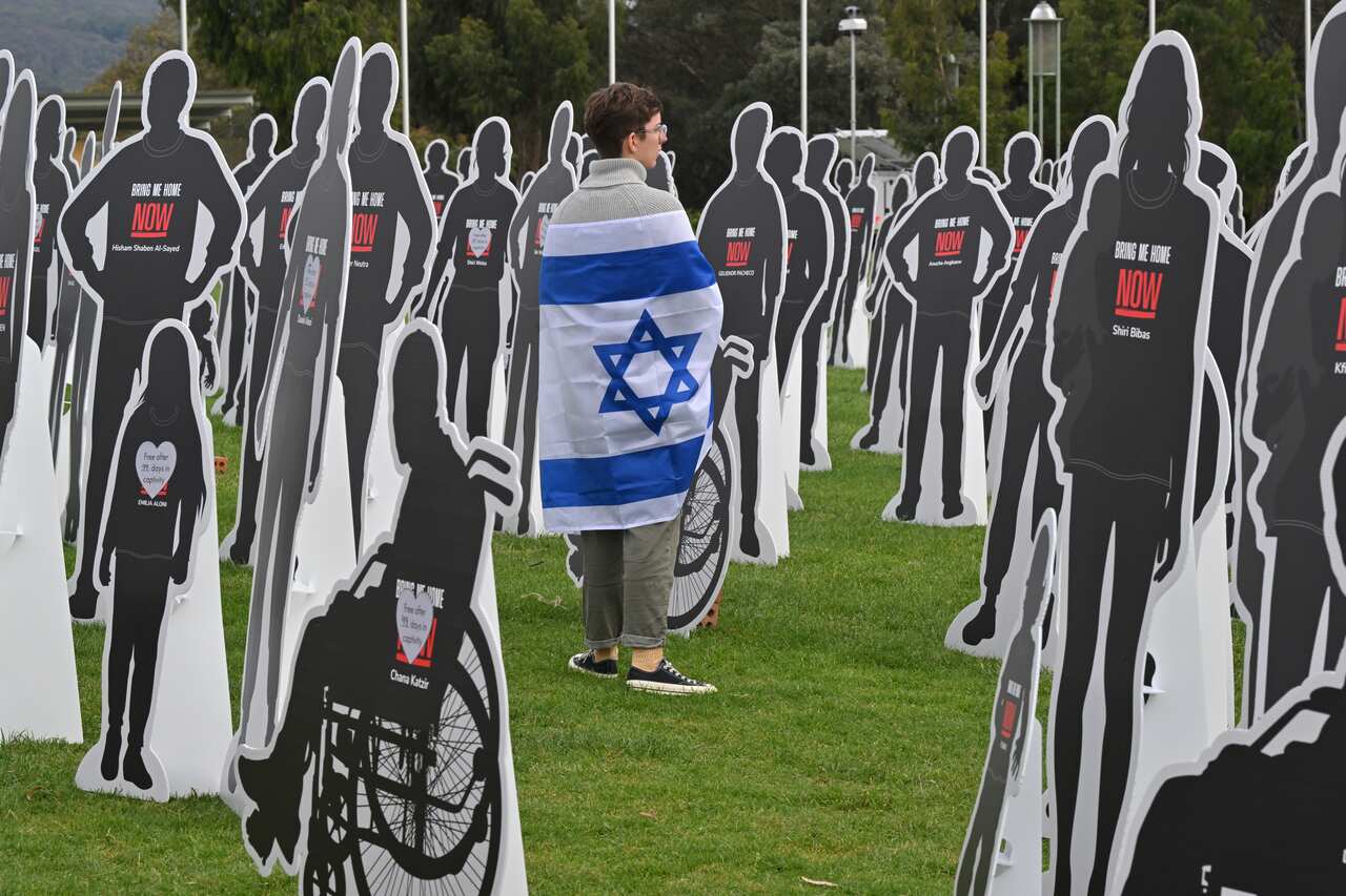A person wrapped in an Israeli flag standing amid cardboard cutouts