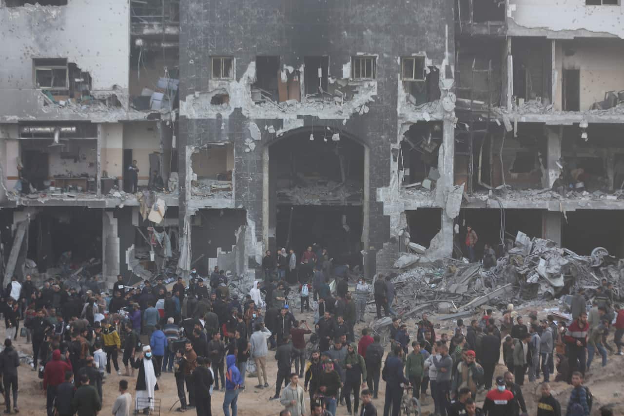 A crowd of people surrounds a burnt, destroyed building.