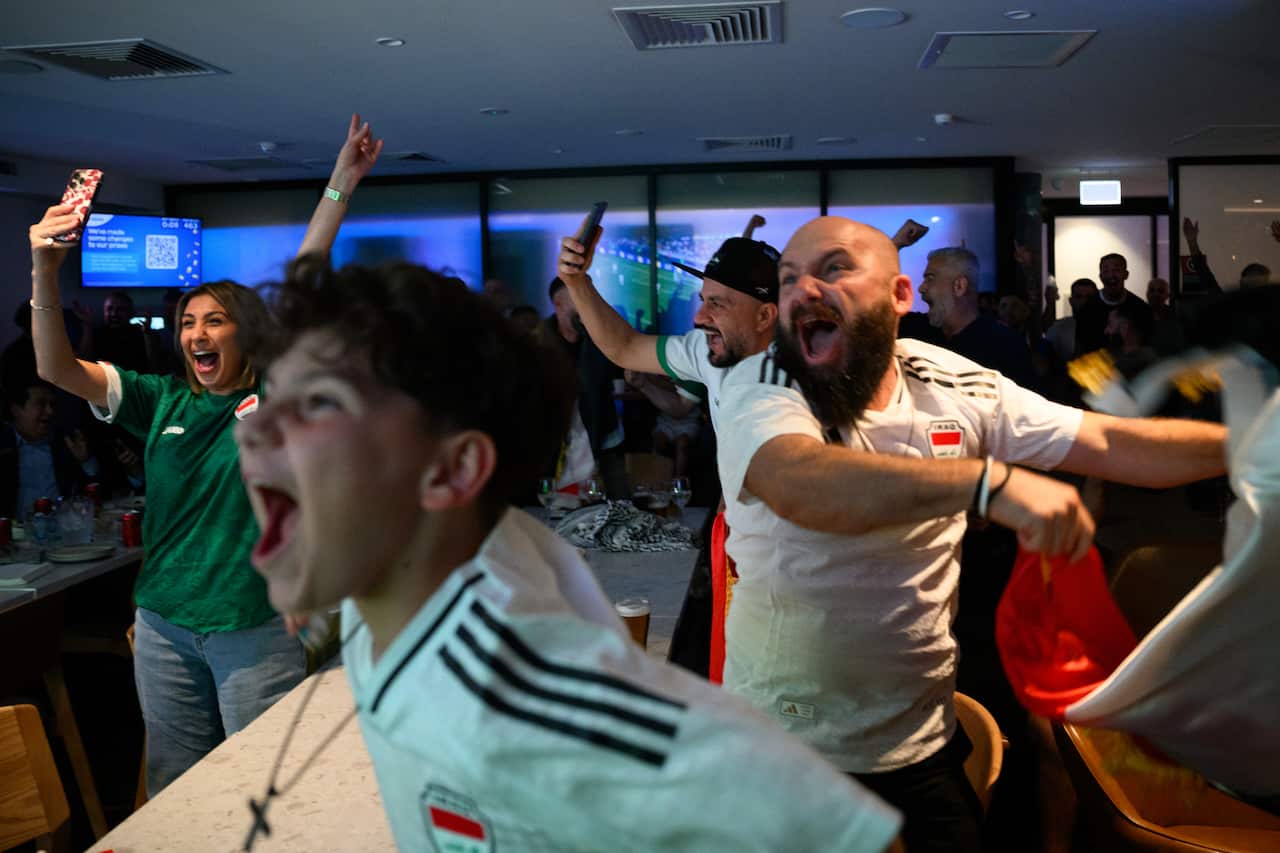 Football fans dressed in jerseys cheer and yell in an indoor setting.