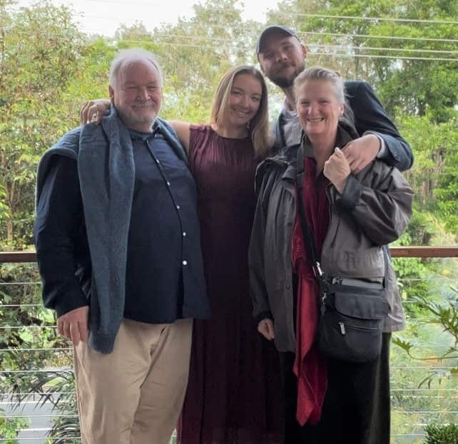 A man stands next to a young woman and a young man, with a woman on the right wearing a grey shirt.