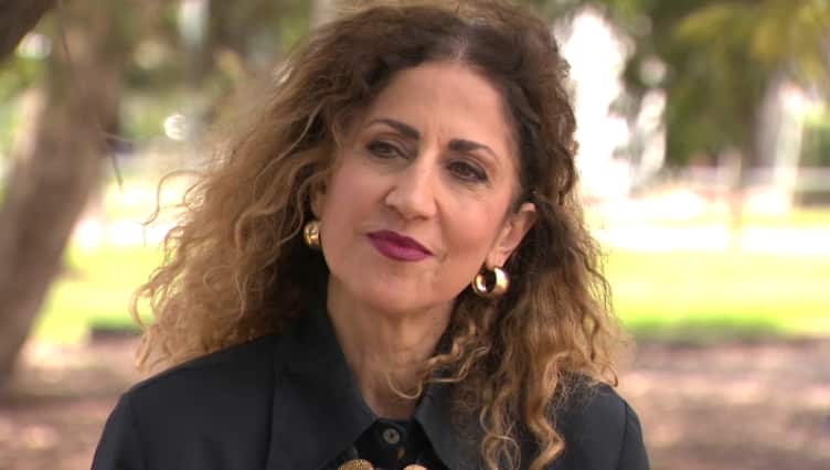 A woman with curly hair and big round earrings is wearing a black jacket.